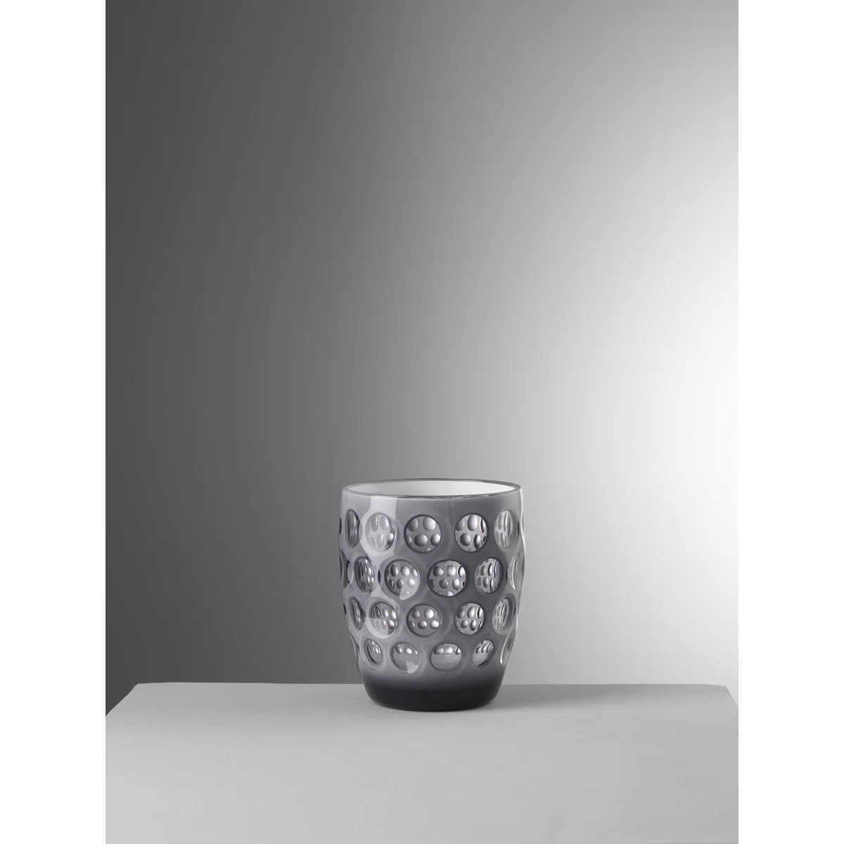 A gray ceramic cup with a glossy finish and a pattern of circular dimples sits on a light gray surface against a gradient gray background.