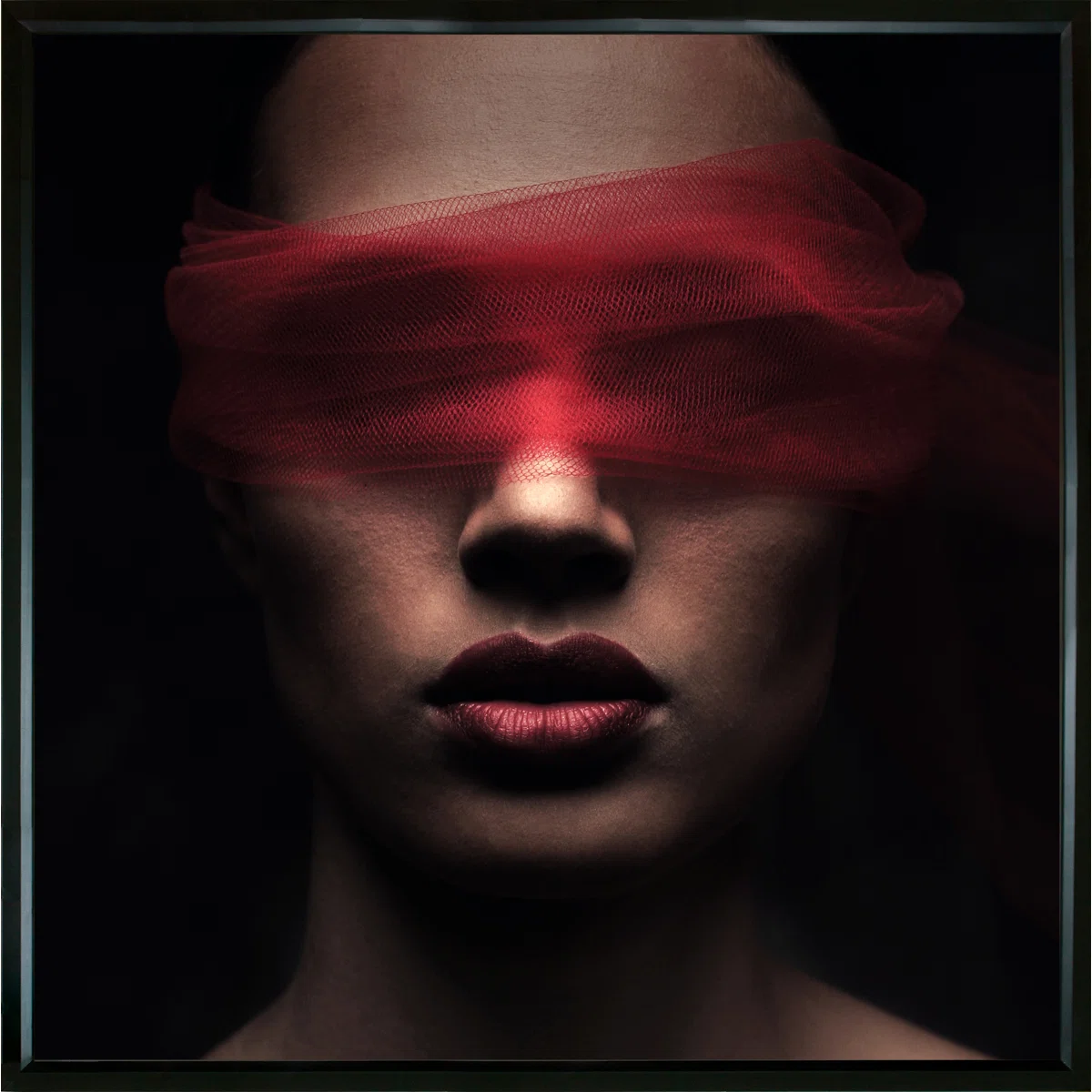 A person with bold lipstick has their eyes covered by a sheer red fabric, partially obscuring their face against a dark background.
