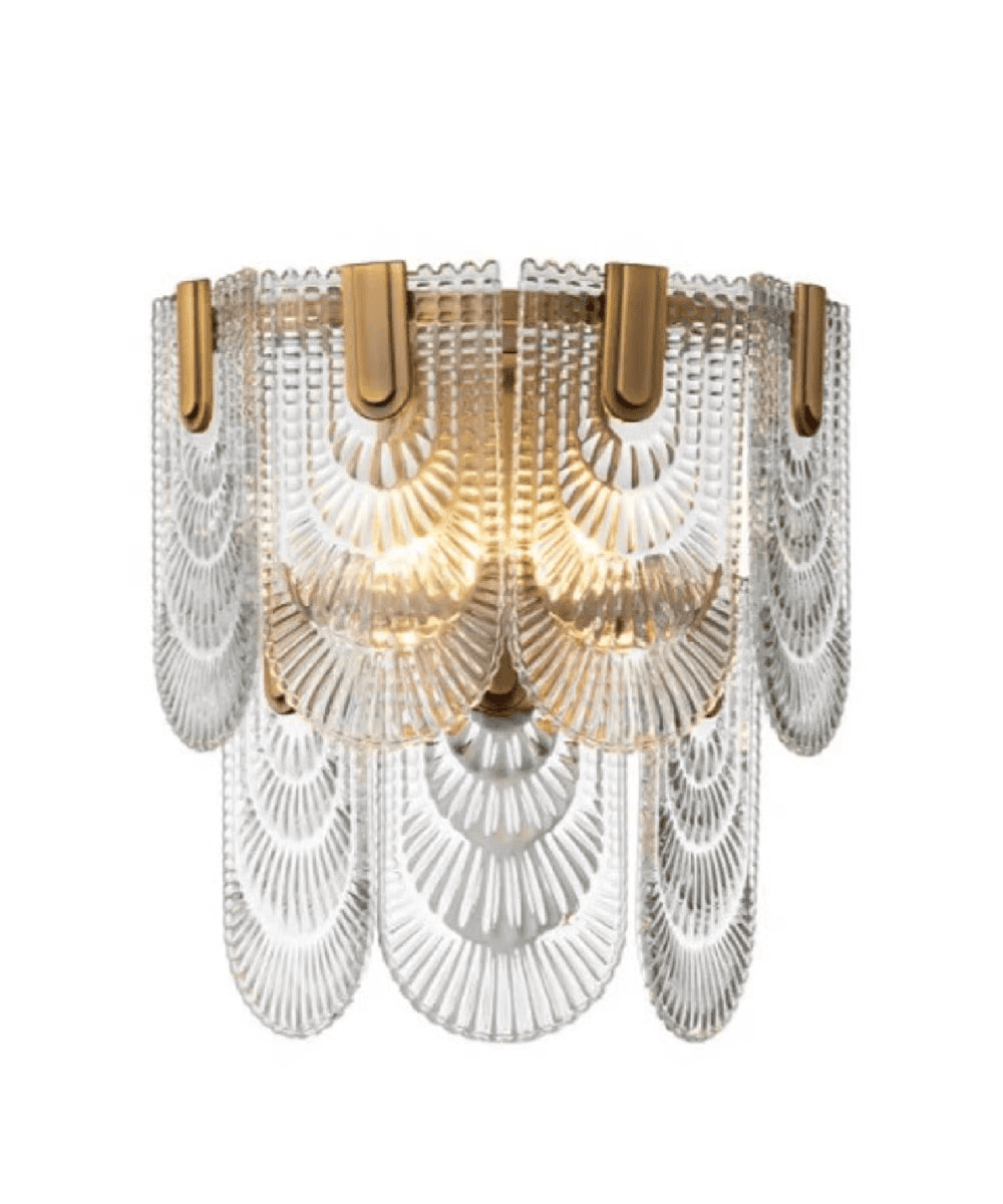 A decorative wall sconce with layered, clear glass panels featuring fan-like patterns and brass accents, illuminated by warm light.