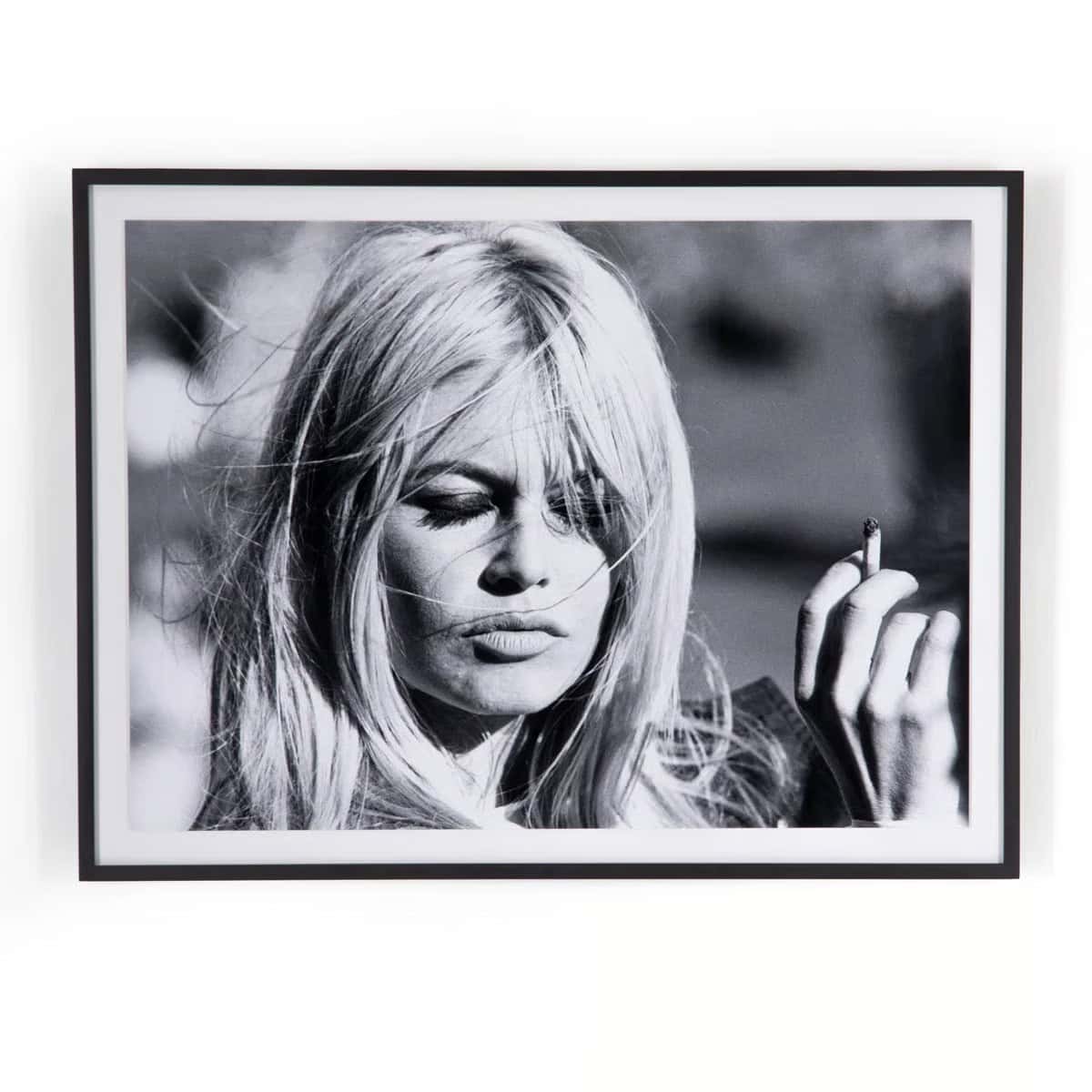 Black and white photo of a woman with long blonde hair holding a cigarette, eyes partially closed, with a thoughtful expression. Framed image with a blurred outdoor background.