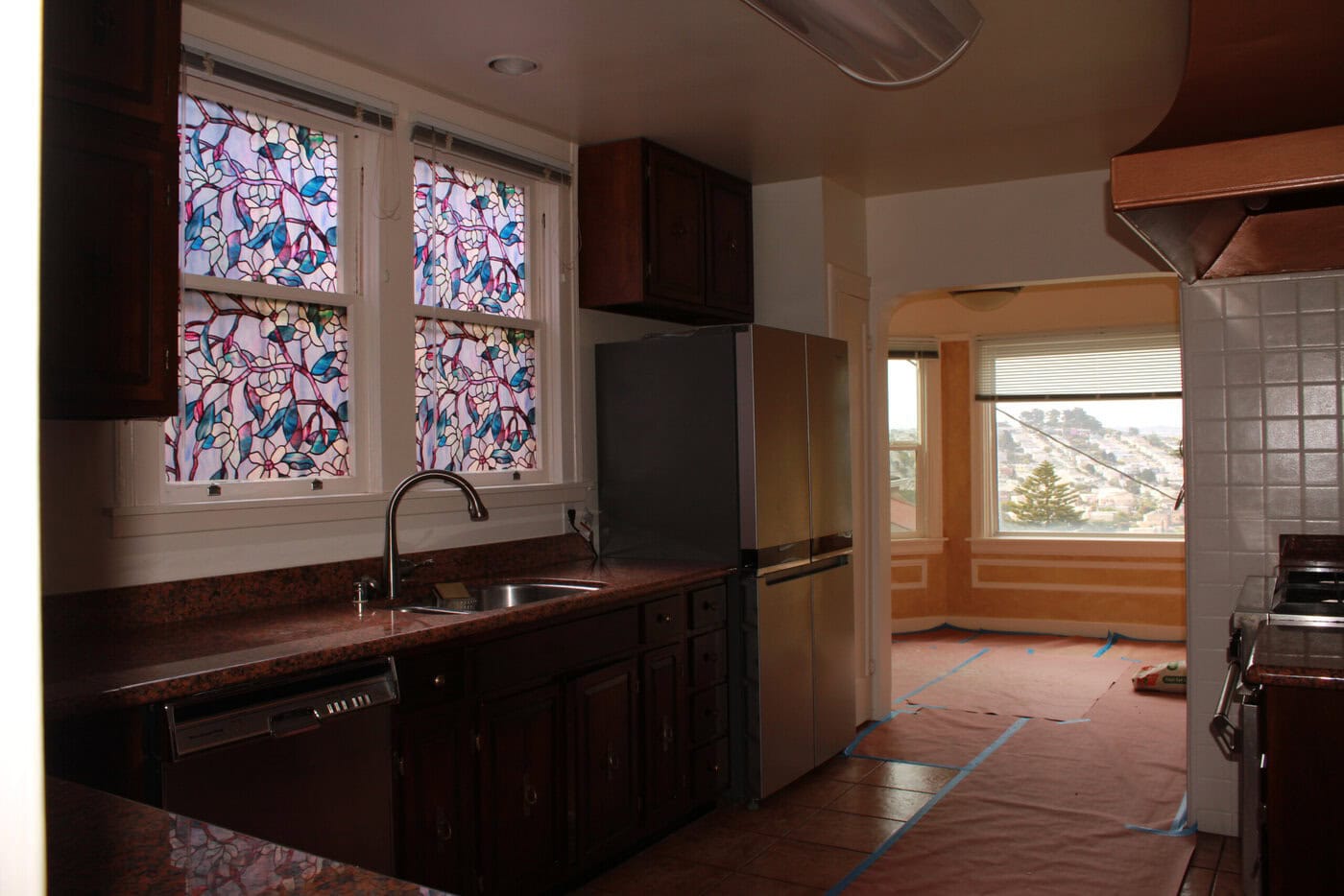 This San Francisco Home Features A Kitchen With Dark Wood Cabinets, Brown Countertops, And A Stainless Steel Fridge. Colorful Stained Glass Windows Above The Sink And An Upgraded Dining Area With Large Windows Create A Welcoming Space.