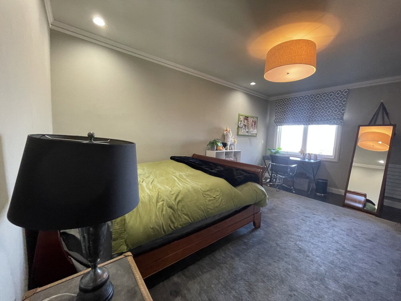 A Cozy San Francisco Bedroom With A Bed Covered In A Green Comforter, A Black Lamp On A Side Table, A Floor Mirror, And More—Perfect To Sell As-Is Or Update With Help From A Contractor.