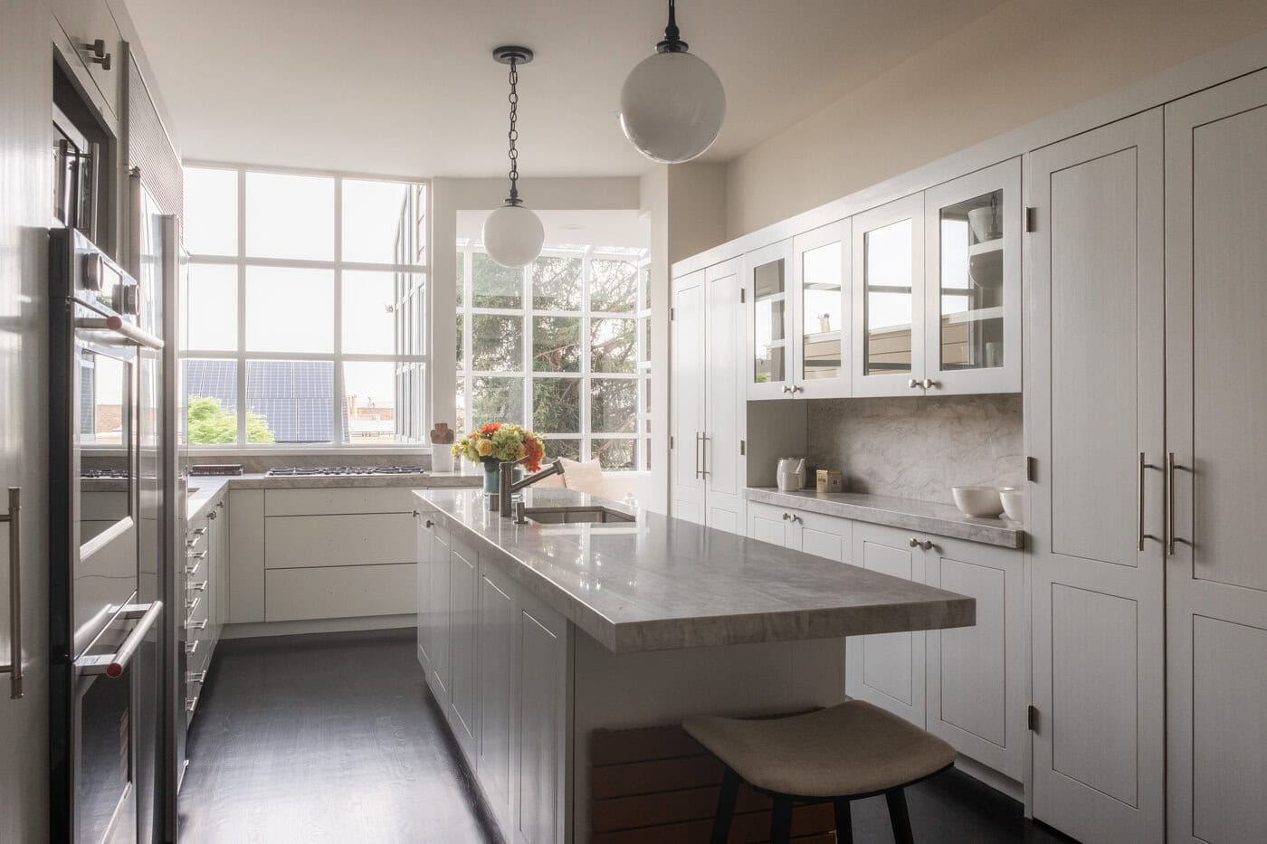 Bright, Modern Kitchen With White Cabinets, Marble Countertops, A Central Island With A Stool, Pendant Lights, And Large Windows Letting In Natural Light—Perfect For Your Next San Francisco Upgrade. A Vase With Flowers Sits On The Island.