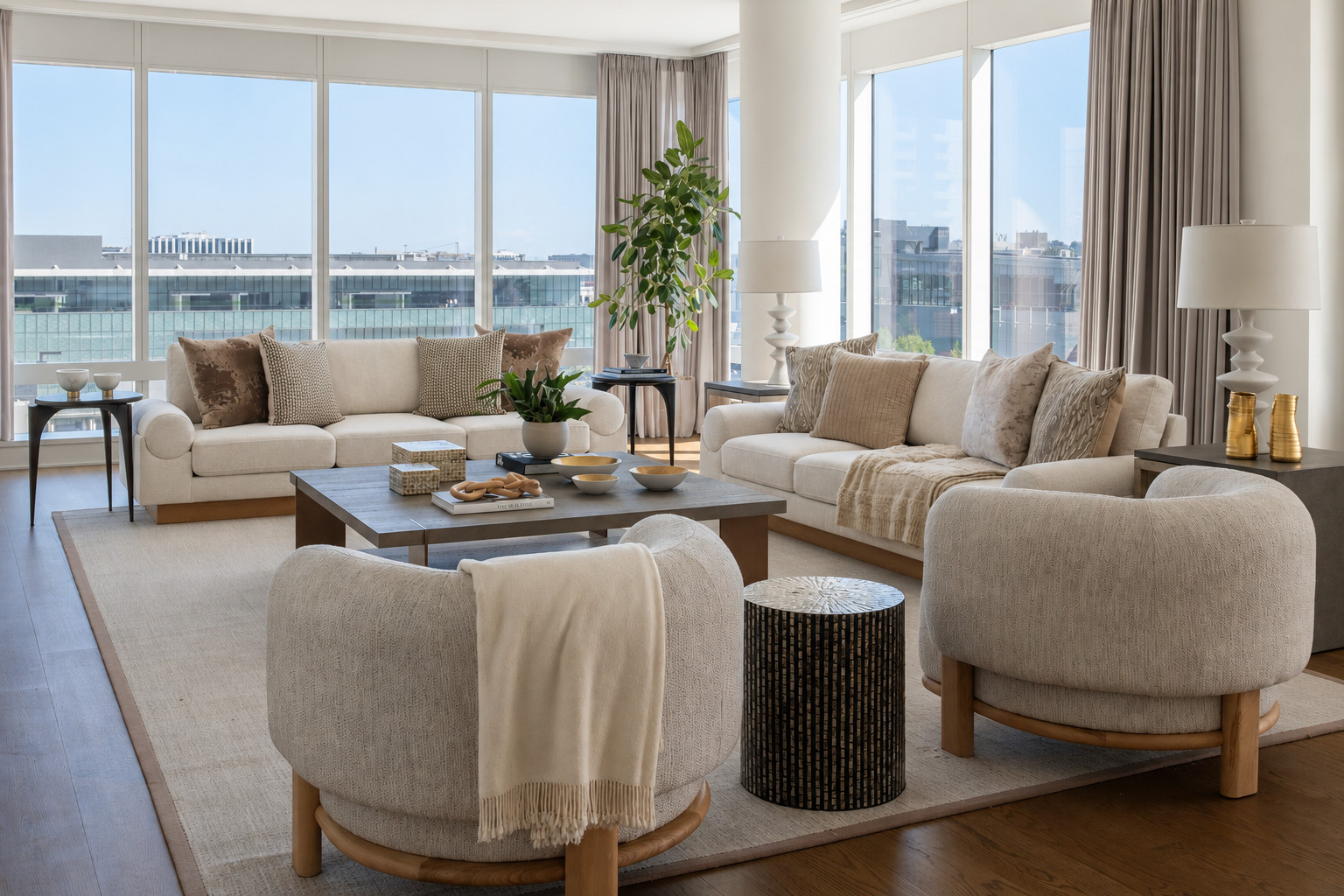 Bright Modern Living Room With Large Windows, Two White Sofas, Two Round Armchairs, A Coffee Table, Decorative Plants, Neutral Tones, And City Views Outside.